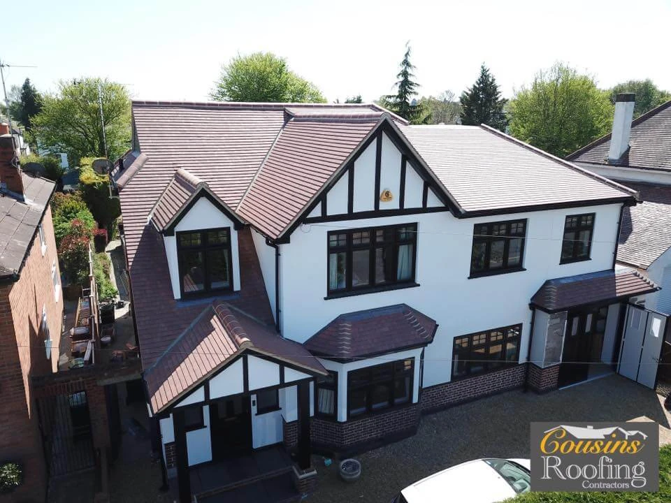 Aerial view of a completed tiled roof on a white Tudor-style house with multiple gables