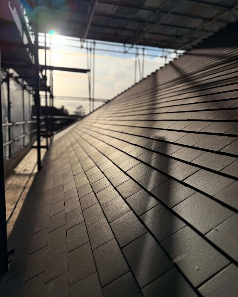 Newly laid dark grey slate tiles on a pitched roof with scaffolding in place