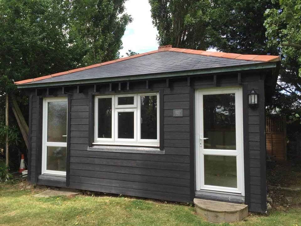 Black timber garden cabin with a newly slated pitched roof and terracotta ridge tiles