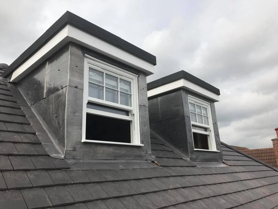 Two slate-clad dormers with white sash windows set into a slate tiled roof