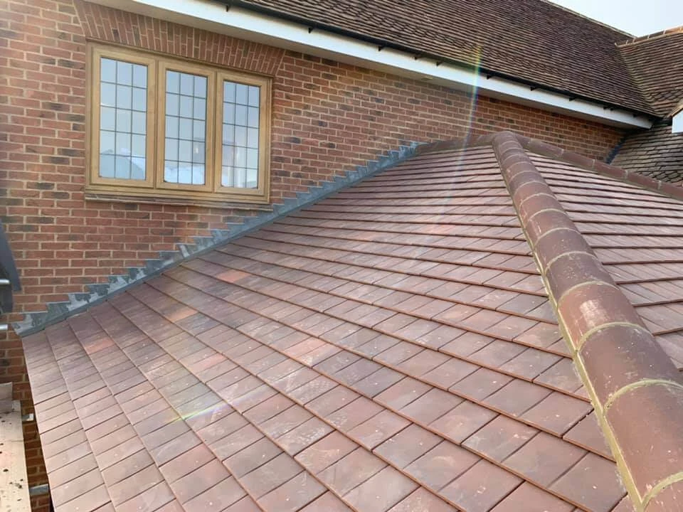 Newly completed hipped roof with reddish-brown clay tiles on a red brick house